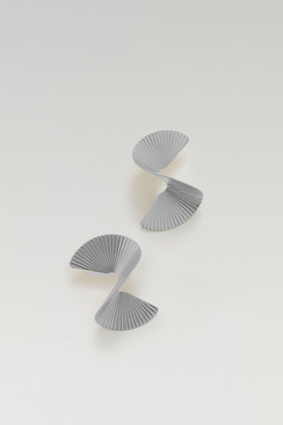 A pair of modern, sculptural gray pleated earrings with a spiral design, displayed on a clean, light off-white background.