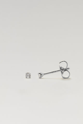 A single silver stud earring with a clear gemstone, shown next to its butterfly backing on a light gray background.