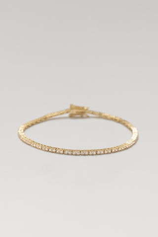 Clara mini tennis bracelet, gold plated, lying in a loose circle with the clasp at the top