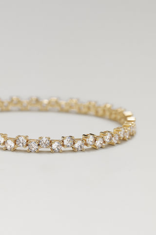 Ramona tennis bracelet, gold plated, angled view of the staggered stone rows on a pale surface