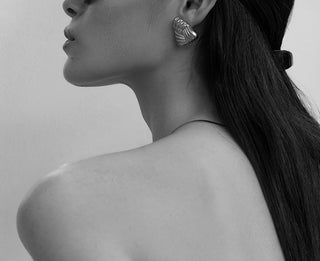 A black and white image of a woman from the side with bare shoulders. She has long dark hair and is wearing an earring from One Dame Lane's fashion jewellery. 