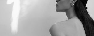 A black and white image of a woman from the side with bare shoulders. She has long dark hair and is wearing an earring from One Dame Lane's fashion jewellery. 
