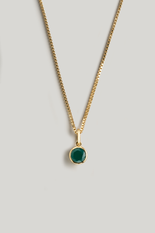 A gold chain necklace with a small round bezel-set green gemstone pendant, displayed against a solid light gray background.