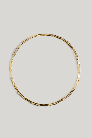 A gold-toned geometric link chain necklace arranged in a circle on a solid light gray background.