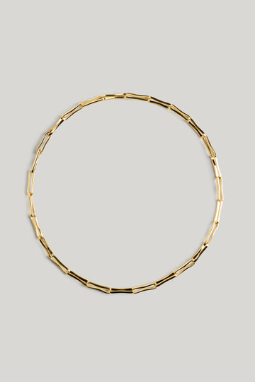 A gold-toned geometric link chain necklace arranged in a circle on a solid light gray background.