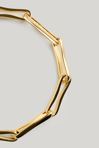 A close-up of a polished gold-tone chain link bracelet on a light gray background.
