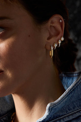 Sabine earring on the ear with two pear-shaped stone studs and a small flower stud, over a denim collar