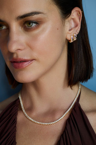 Model with a dark bob in a burgundy halter top wearing the gold-tone Vida tennis necklace and stone-set huggie hoops