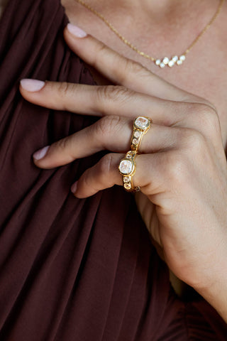 Two gold plated Mara rings worn on one hand against a burgundy top, with a bezel-set stone necklace