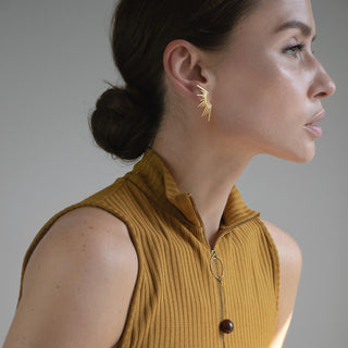 Sunset gold stud earrings worn on the ear with a radiant fan silhouette